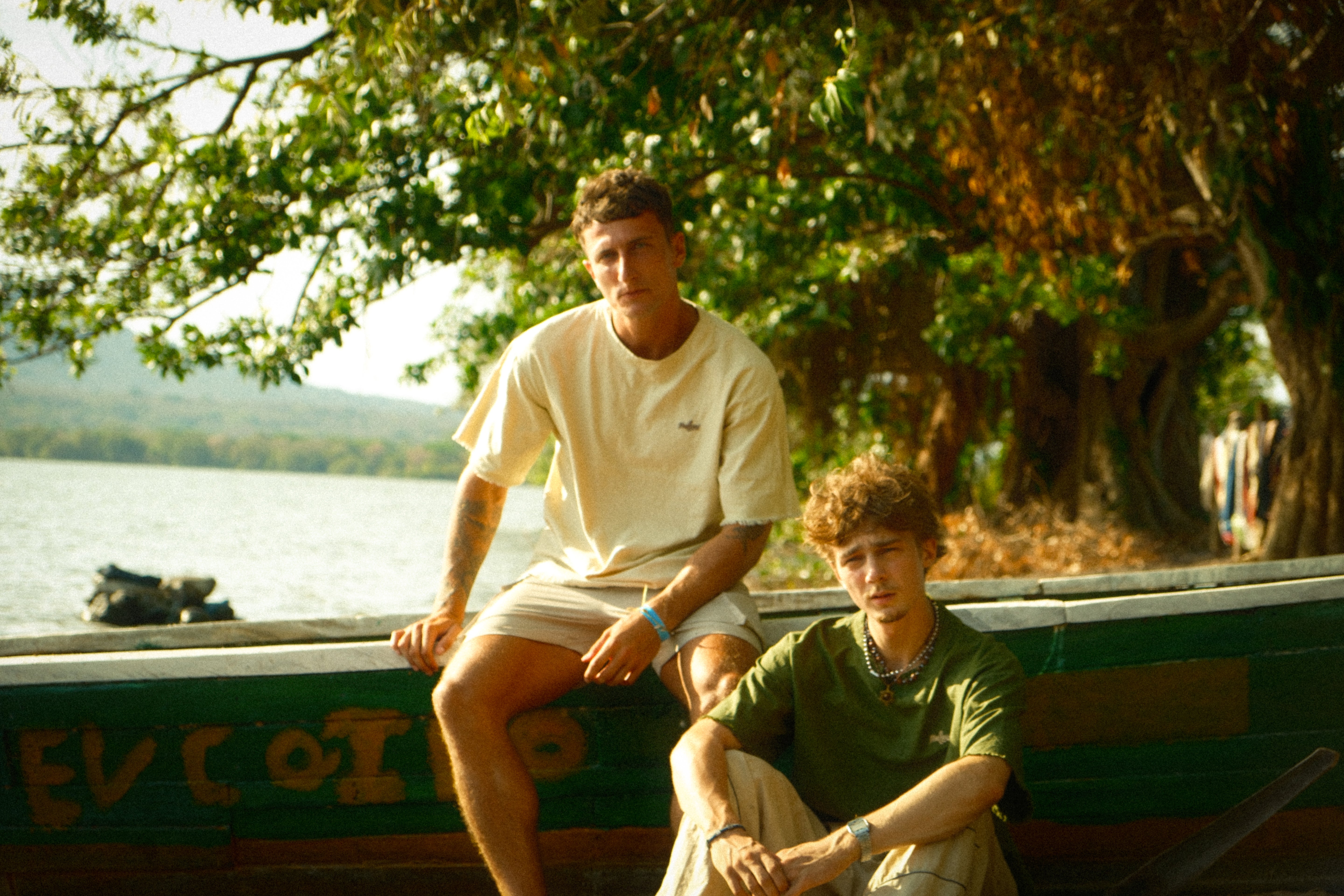 Two people sitting on a boat by a body of water with trees and mountains in the background wearing hemp.