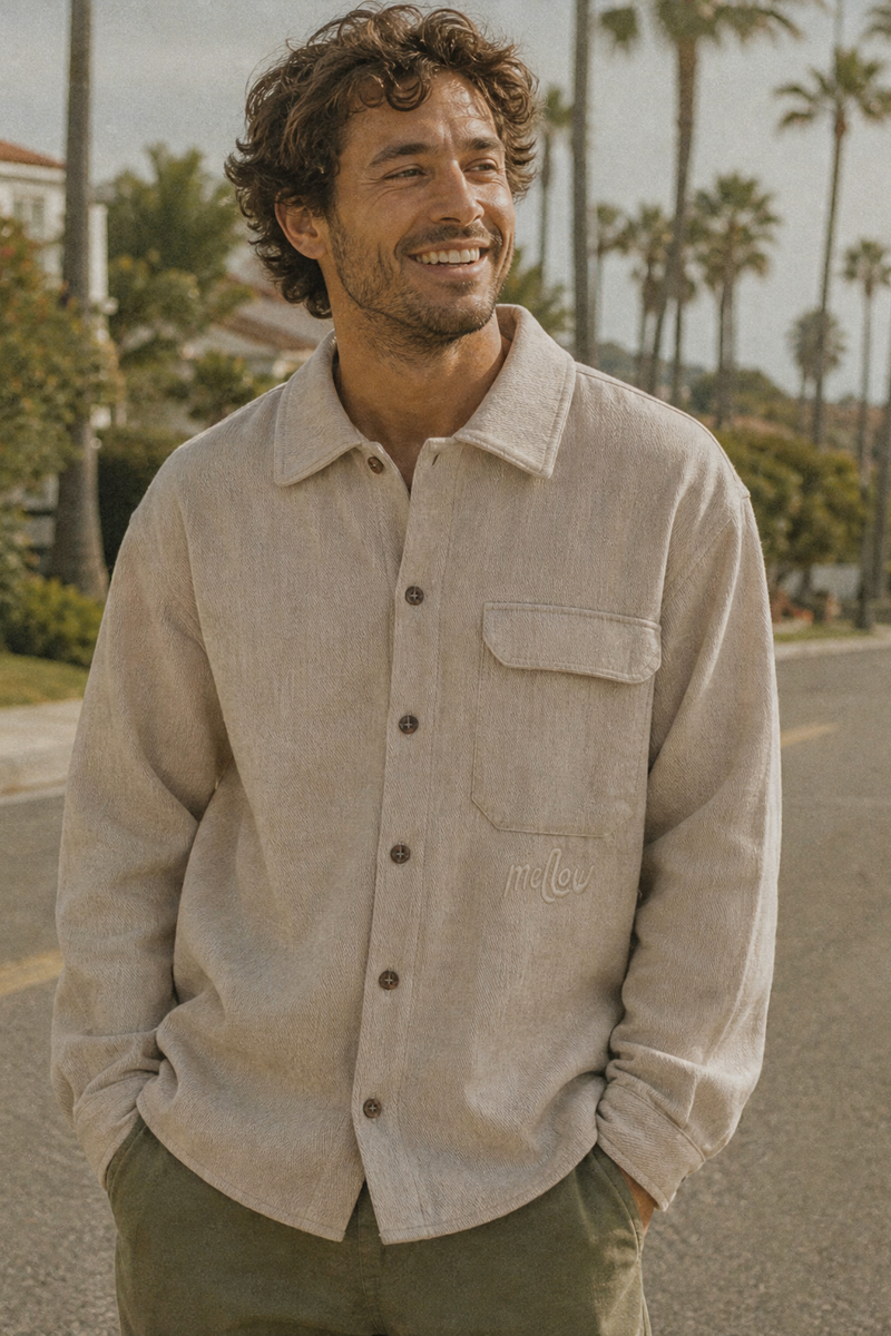 Man standing with a hemp jacket on a street with palm trees and a house in the background