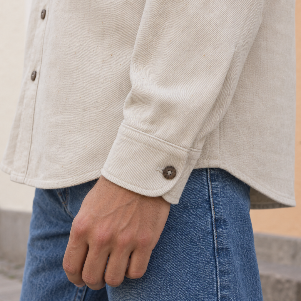 A close-up of a person wearing a light beige hemp button-up shirt and blue jeans, standing outdoors in front of a building.